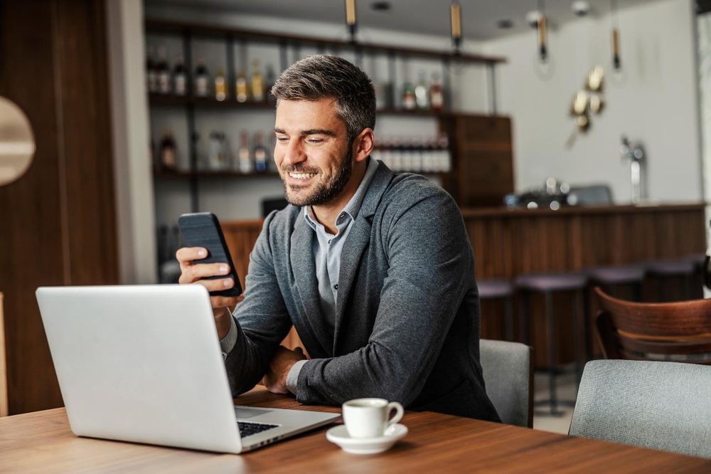 A personal loan broker on his phone in front of a laptop in a cafe setting