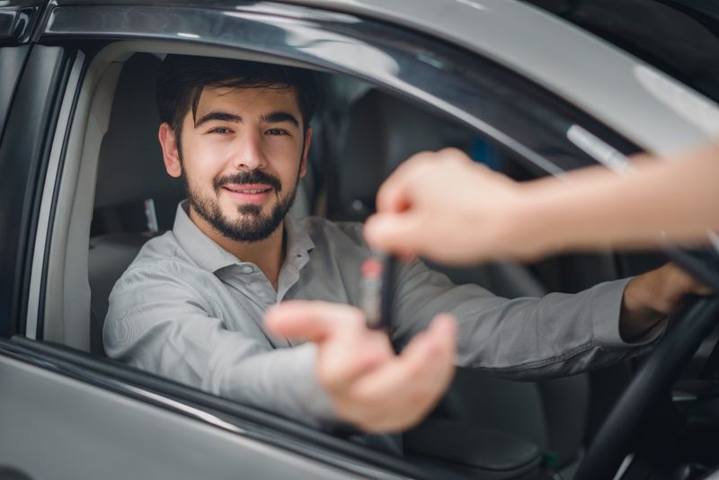A man in a car receiving keys to a vehicle after signing a novated lease